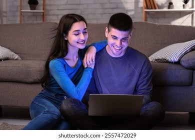 Couple shopping online on laptop, discussing purchase sitting on floor in cozy living room - Powered by Shutterstock