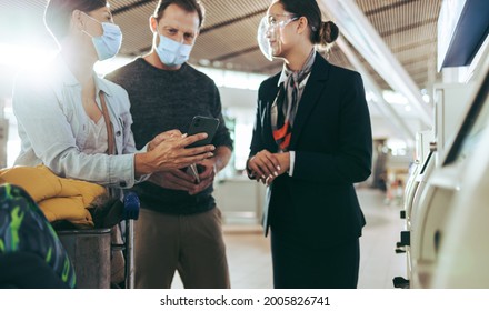 Couple Showing Mobile Phone To Airport Staff During Pandemic. Tourist Family Taking Help Of Ground Attendant At Airport In Pandemic.