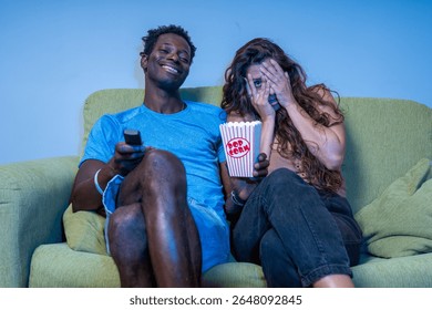 A couple shows different reactions while watching a horror movie; the woman is scared and the man is amused.