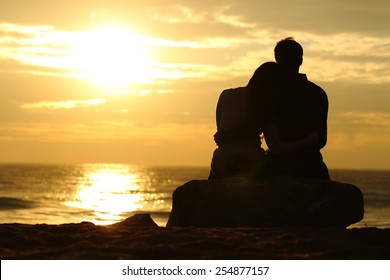 Couple silhouette cuddling and watching sun at sunset on the beach