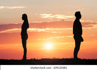 Couple Silhouette Standing Away From Each Other Against Dramatic Sky At Sunset