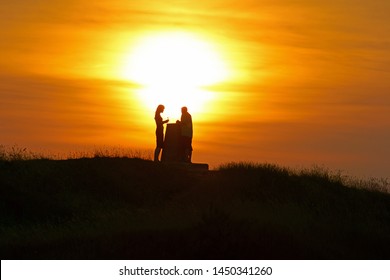 A Couple Silhouetted At Sunset On Painswick Beacon In Summer, The Cotswolds, Gloucestershire, England, UK