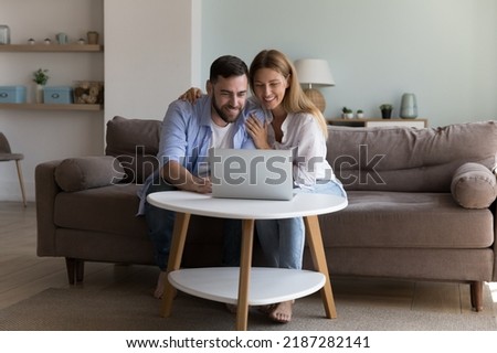 Couple sit on sofa with laptop buying goods, make remote order, enjoy easy retail commerce services use internet for comfort life. Modern tech, booking hotels, planning family holidays on-line