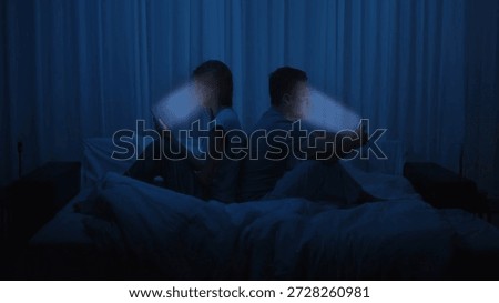 A couple sits back to back in bed, both illuminated by the glow of their smartphone screens. Addiction to gadgets and social media, digital isolation, relationship alienation, and technology overuse.