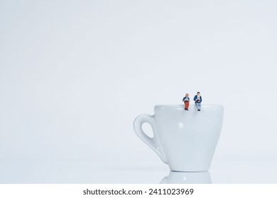 A couple sits reading on a white coffee cup, white background, miniature figure scene - Powered by Shutterstock