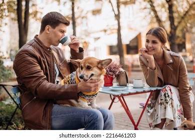 A couple sits in a street cafe with corgi dogs. - Powered by Shutterstock