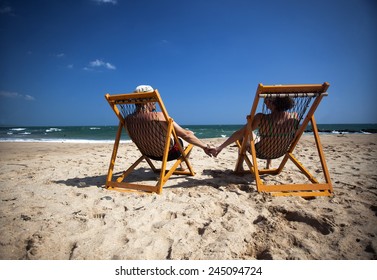 Couple sitting in beach chairs and holding hands on a tropical beach