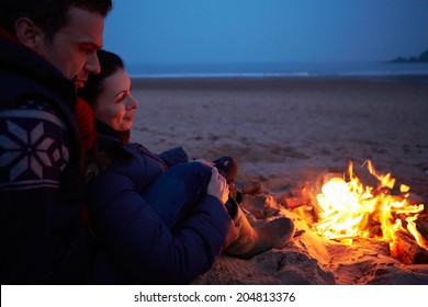 Couple Sitting By Fire On Winter Beach