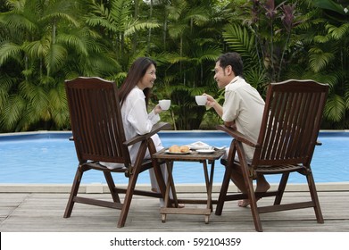 Couple sitting by swimming pool, have drinks, looking at each other - Powered by Shutterstock