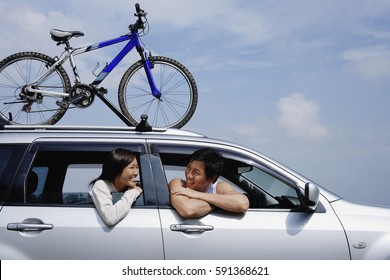 Couple sitting in car, leaning out of the windows, bicycle on the roof
