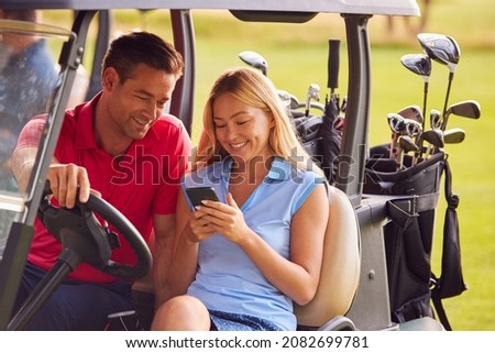 Couple Sitting In Golf Buggy On Course With Woman Using Mobile Phone