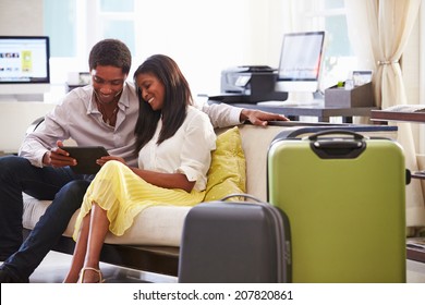 Couple Sitting In Hotel Lobby Looking At Digital Tablet