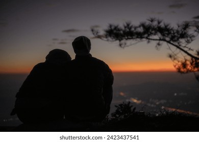 A couple sitting huddled and watching the sunrise or sunset. silhouette at sunrise. - Powered by Shutterstock