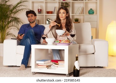 Couple Sitting In The Living Room, Having Dinner And Watching TV.