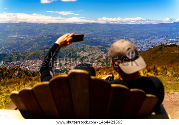 Couple sitting on a bench on top of the mountain\
surrounding Quito, Ecuador. Elevation of 4.1km. Cable car access\
good for hiking