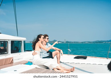 A couple is sitting on a boat in the ocean, pointing to something in the distance. Scene is peaceful and romantic, as the couple enjoys each other's company and the beautiful scenery around them - Powered by Shutterstock