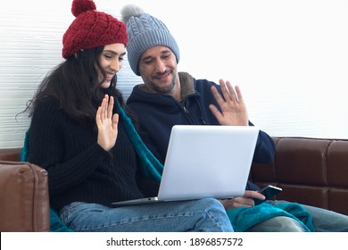 Couple Sitting On Brown Sofa In Living Room And Using Laptop Enjoy Online Conversation (facetime, Webcam, Video Call) And   Waving Hands With Family On Winter Season.