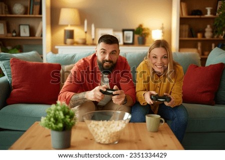 Couple sitting on couch with joysticks and playing video game in living room