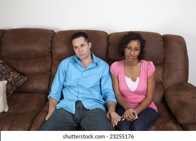 A couple sitting on the couch side by side looking very bored