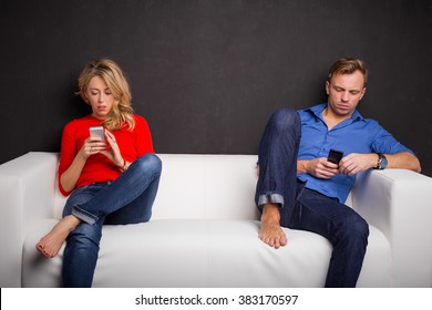 Couple Sitting On Couch With Their Phones In Their Hand 