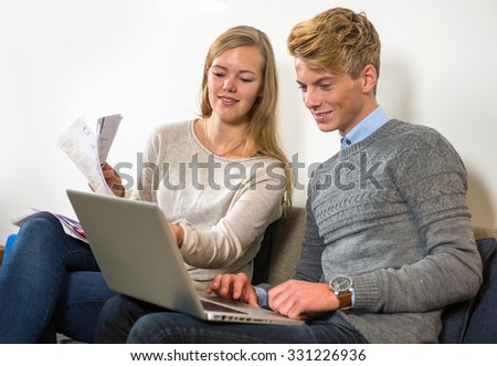 Couple, sitting on a couch, with a woman holding several bills and invoices, comparing their expenditure on the manÃ?Â¢??s laptop with their joint account cash book Stock photo © 