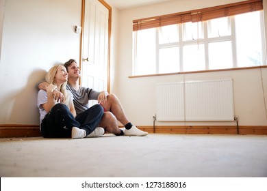 Couple Sitting On Floor In Empty Room Of New Home Planning Design