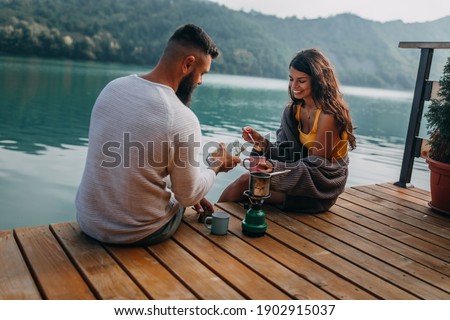 Couple sitting on lake pier and making coffee