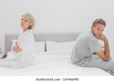 Couple Sitting On Opposite Sides Of Bed Looking At Camera After A Fight