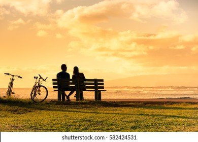 Couple sitting on park bench watching the sunset. 