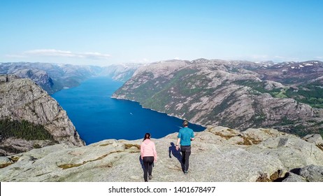 Couple sitting on a rock and admiring a view on Lysefjorden. Areal shot, upper perspective on the couple. Endless view of the fjord. Couple rising hands above their head and forming a heart. Freedom