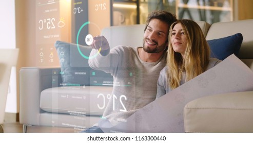 A couple sitting on the sofa controls all the functions of the house such as wi-fi, heating, lighting, television through holography. Concept of, home automation, automations, future, technology. - Shutterstock ID 1163300440