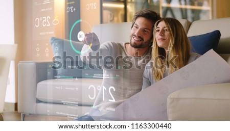 A couple sitting on the sofa controls all the functions of the house such as wi-fi, heating, lighting, television through holography. Concept of, home automation, automations, future, technology.