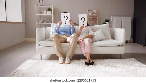 Couple Sitting On Sofa Holding Question Mark Sign In Front Of Face - Powered by Shutterstock