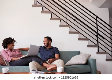 Couple Sitting On Sofa At Home With Woman Using Laptop Computer