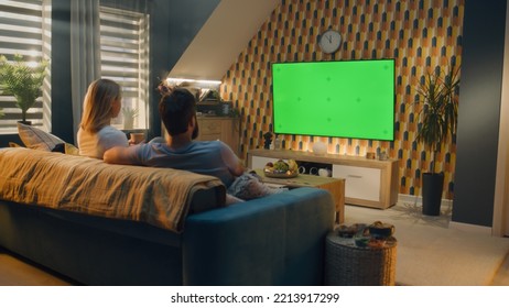 Couple sitting on sofa in living room, talking, watching breaking news, movie or series on TV. Wife and husband resting and chilling at home in the evening together. Green screen. Chromakey. - Shutterstock ID 2213917299