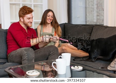 Couple sitting on sofa playing with pet dog smiling