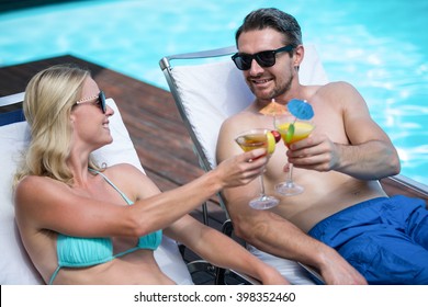 Couple sitting on sun lounger toasting cocktail near the pool - Powered by Shutterstock