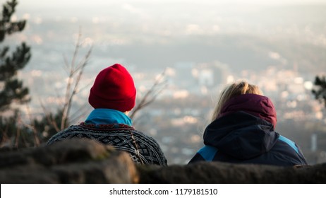A couple sitting on the top of the hill in Oslo, Norway, with the view on downtown. Wintertime right before sunset.