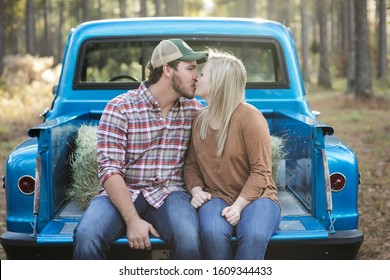 Couple Sitting On A Vintage Blue Pick-up Truck Bed Kissing