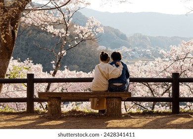 A couple sitting on a wood bench under Sakura trees, enjoying the panoramic view and Hanami (a leisure activity of admiring cherry blossoms in spring), in Takato Castle Ruins Park, Ina, Nagano, Japan - Powered by Shutterstock