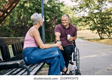 Couple sitting in park while drinking coffee, man is in the wheelchair.  - Powered by Shutterstock