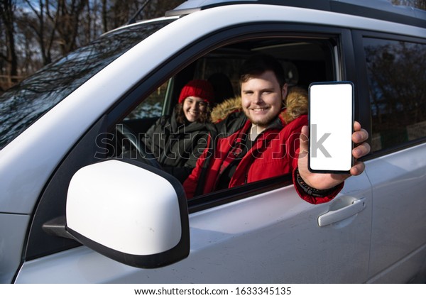 couple sitting in rent car man holding phone with\
white empty screen