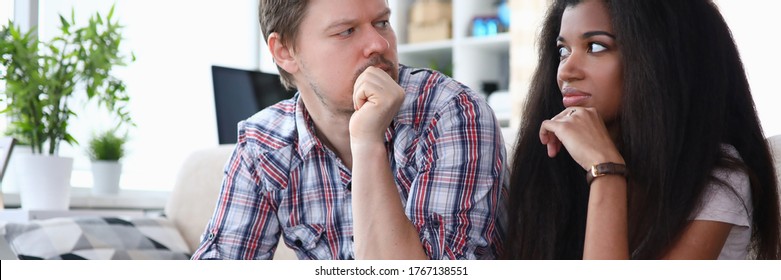 Couple Sitting Sofa At Home Looking At Each Other. Tensions Between Spouses, Unwillingness To Compromise. Woman Does Not Agree With Decision Man. Family Troubles Over Online Shopping