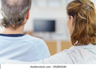 Couple Sitting Watching Television At Home With A View From Behind Between Their Heads