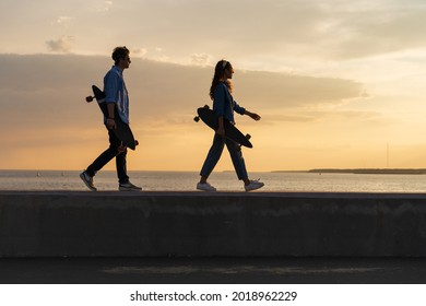 Couple of skateboarders walking on seaside carrying longboards at sunset. Silhouettes of two trendy skateboarders wear stylish urban style clothes enjoy sea view. Hipster lifestyle and freedom concept - Powered by Shutterstock