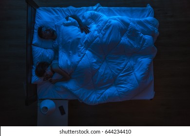 The Couple Sleeping On A Bed. Evening Night Time. View From Above