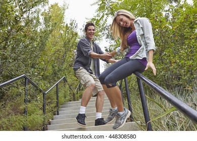 Couple Sliding Down Step Railing In Forest