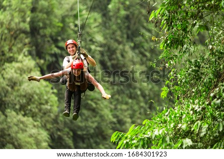 A couple sliding on a zipline through the lush canopy of Ecuador while a crowd watches in awe, with an extreme shower of adrenaline rushing over them.