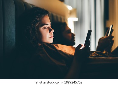 Couple with smartphones in their bed. Mobile phone addiction. Bored distant couple ignoring each other lying in bed at night while using mobile phones. - Powered by Shutterstock