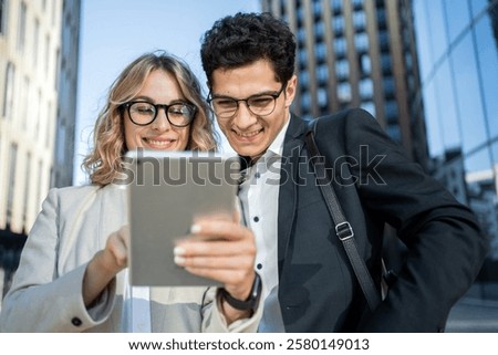 Couple smiles while using a tablet outside a modern building in urban setting during daytime